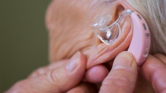 hands holding a hearing aid in an older person's ear