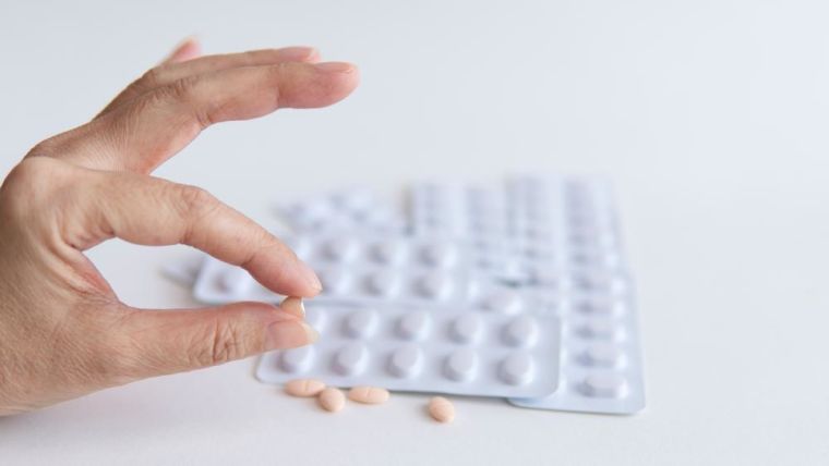 Half of statins tablets pill in female patient hand and white blister pack of them for light resistance packaging on white background
