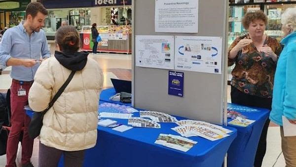 Two members of the public chatting to researchers at an information stand in a shopping centre