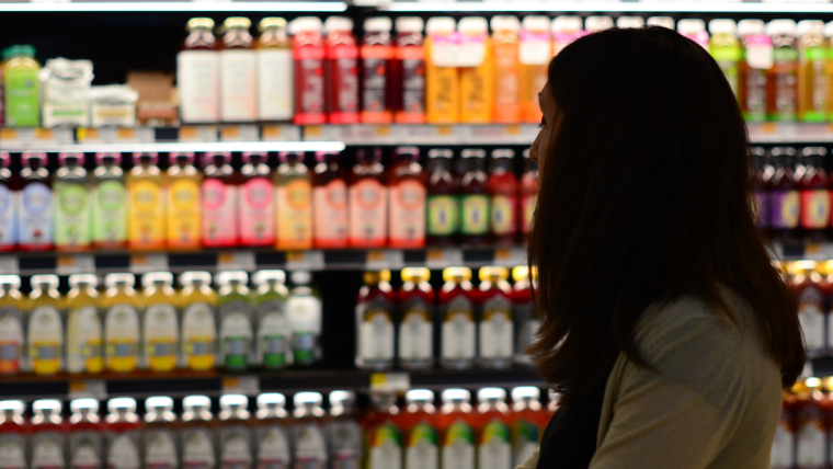 Photograph of a woman with long brown hair in a store looking at brightly lit shelves of bottled drinks